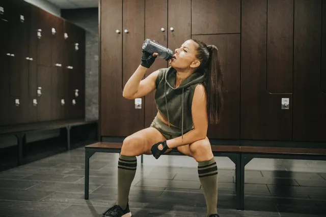Mulher bebendo da coqueteleira no vestiário da academia